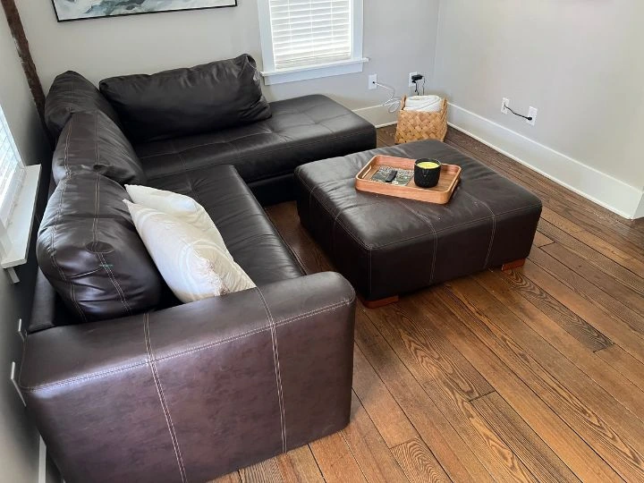 A bright and inviting residential living room after a professional cleaning. The plush sofa and armchairs are clean and free of dust. The coffee table is polished, and the area rug is freshly vacuumed. The windows are sparkling clean, allowing natural light to fill the room